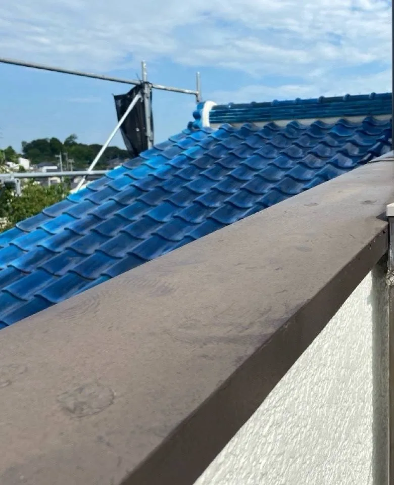 バルコニーの手すり壁の上にかぶせた板金の笠木と、その奥に見える瓦の下屋根
