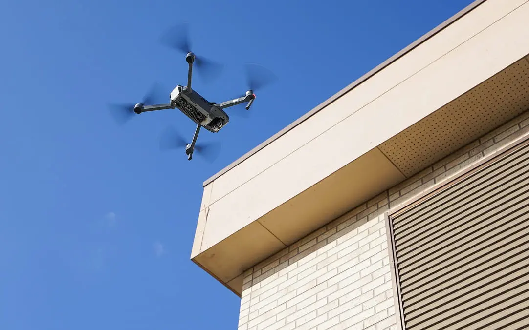 青空の下、住宅の屋根付近を飛行中のドローンの様子