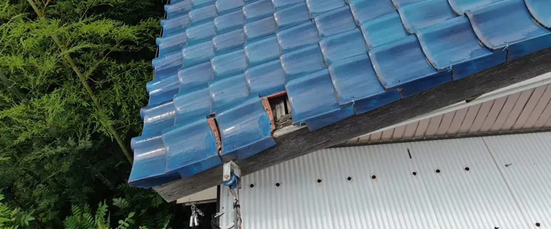 青い瓦屋根の一部が外れ、下地が露出している状態の写真