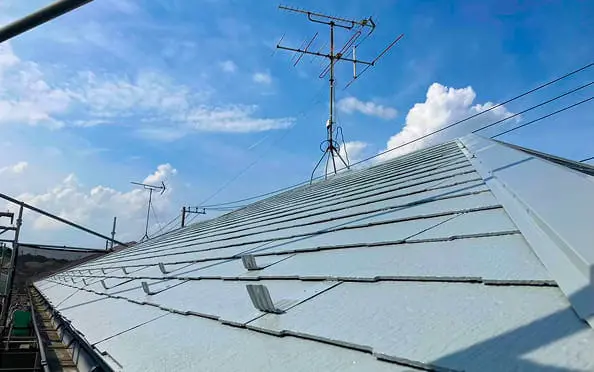 アンテナが立つ青空の下、金具付きのスレート屋根を近接で写した写真