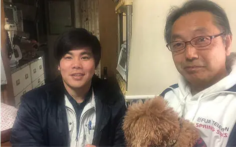 室内で若い男性と中年の男性が小型犬を抱えて並んでいる