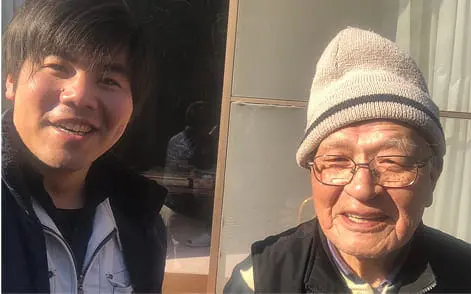 若い男性と高齢の男性が屋外で笑顔を見せているツーショット
