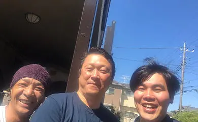 晴天の下で男性3人が外で肩を並べて笑顔を見せている