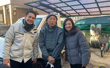 屋外で高齢男性と若い男女が防寒着を着て並んでいる写真