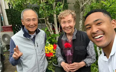 庭先で年配の夫婦と若い男性が一緒に笑顔で写っている