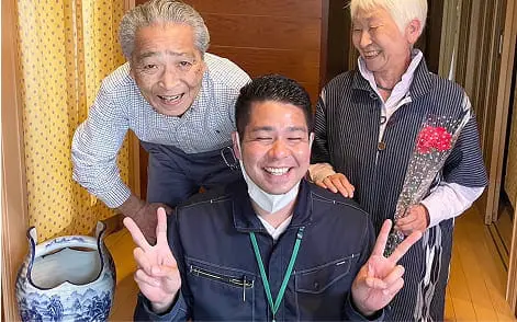 室内で年配の男女と若い男性が並び、笑顔でポーズを決める