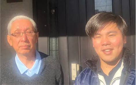 白髪の男性と若い男性が玄関先で並んでいる明るい日差しの中の写真