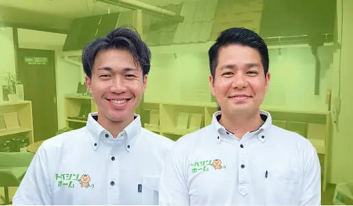 室内背景の前で並んで立つ、白い制服を着た2人の男性スタッフの写真