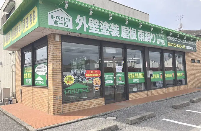 「トベシンホーム 外壁塗装 屋根 雨漏り専門店」と掲示された緑の看板の店舗